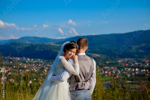 Newlyweds smile and hug each other among the meadow on top of the mountain. Wedding walk in the woods in the mountains, the gentle emotions of the couple, photo for Valentine's Day