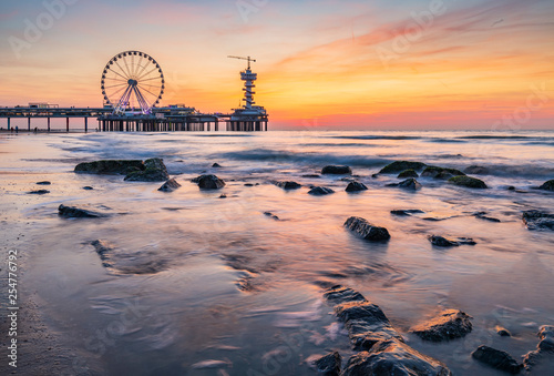 Fotografia Colorful sunset on coastline, beach, pier and ferries wheel, Scheveningen, the Hague