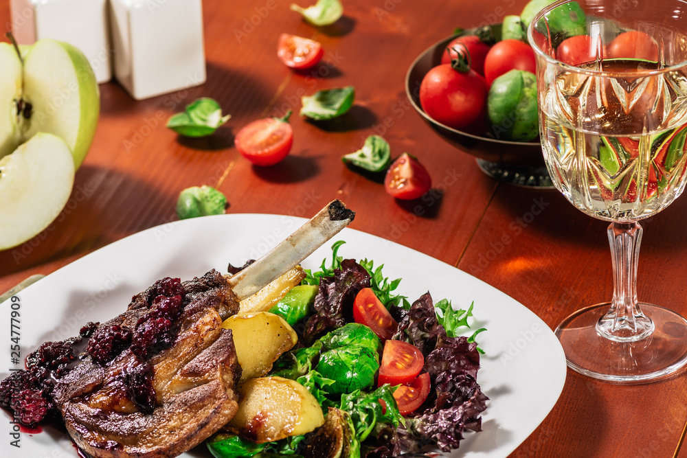 Roasted ribs in blackbarry sauce with vegetables, brussels sprout, cherry tomatoes and apple on wooden background