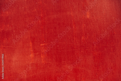 Imperfect metallic plate. Scratched vivid red paint surface close-up. Damage texture in macro. Grungy metal panel. Textured background. Stains on rough faded uneven concrete wall. Old bright red paint