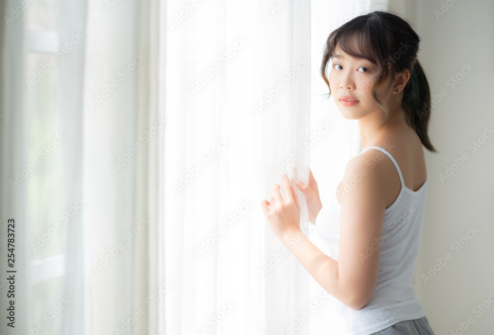 Portrait of beautiful young asian woman standing at the window and smile while wake up with sunlight at morning, girl happy with fresh and cheerful, lifestyle and relax for wellness concept. Portrait of beautiful young asian woman standing at the window and smile while wake up with sunlight at morning, girl happy with fresh and cheerful, lifestyle and relax for wellness concept.