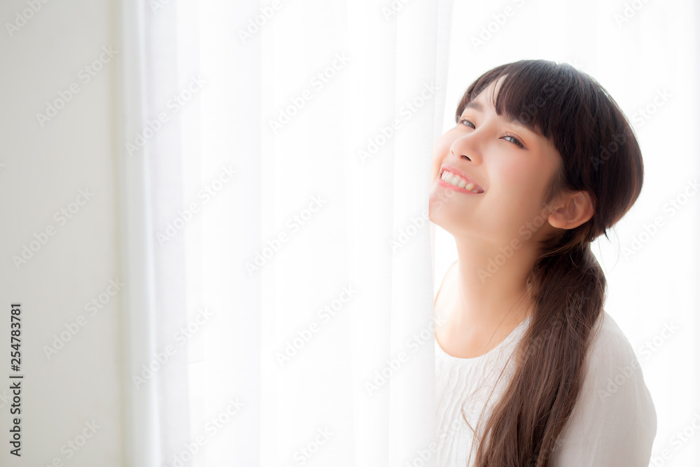 Portrait of beautiful young asian woman standing the window and smile while wake up with sunrise at morning, girl happy with freshness and cheerful, lifestyle and relax concept.