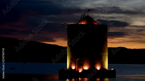 An ancient windmill with romantic lights on the sea bay at sunset
