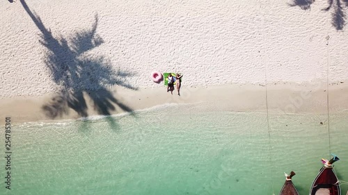 Young brazilian couple laying down on a tropical beach with the brazilian flag on the sand, coconut tree, crystal clear water and local boats