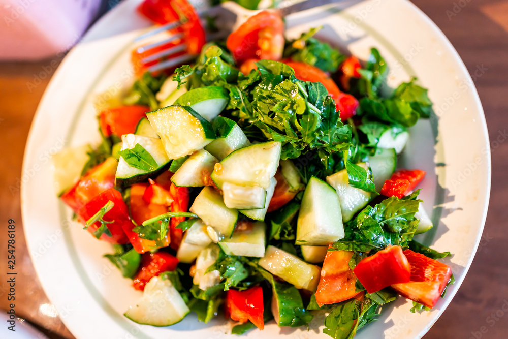 Closeup flat top of fresh green cucumbers on plate with vibrant color salad tomatoes and red bell peppers with parsley and chopped arugula from homegrown garden Closeup flat top of fresh green cucumbers on plate with vibrant color salad tomatoes and red bell peppers with parsley and chopped arugula from homegrown garden
