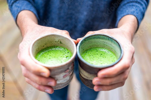 Closeup of man person hands holding two tea cups outside on backyard deck wooden bokeh background in garden drinking matcha green drink photo