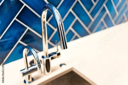 New modern faucet and kitchen sink closeup with countertop, blue vibrant backsplash and shiny clean stainless steel handle