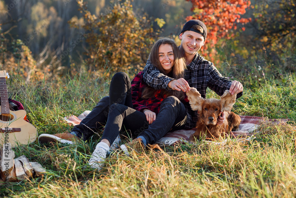 Young couple playing with their pet dog on picnic at park. Woman and woman having fun with dog at park.