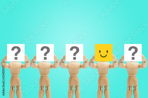 One wooden figure mannequin holding face emotion in happiness and other figures holding question mark in hand.