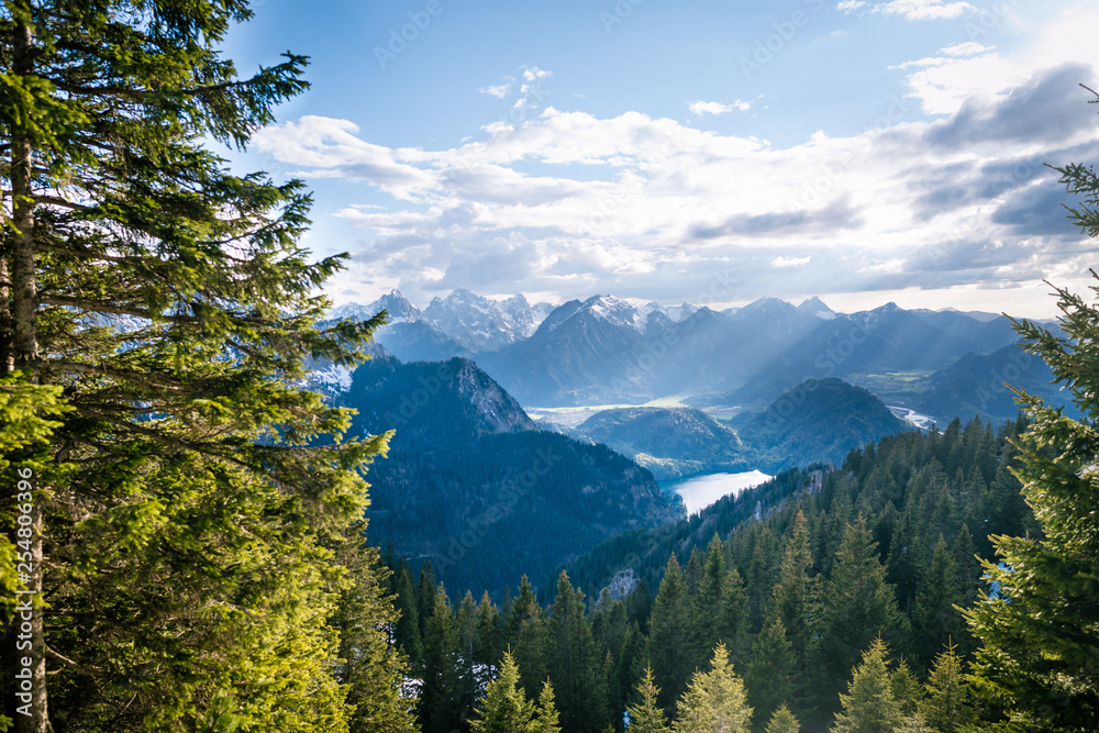 Scenic landscape overlooking the mountains with snowy tops. Sunlight rays falling through the clouds on beautiful valley with lakes and forest.