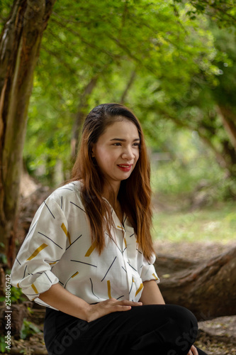 Women white skin lovely brown hair red lip wear white shirt wearing black pants women sit poses photography portrait under the tree In the garden.
