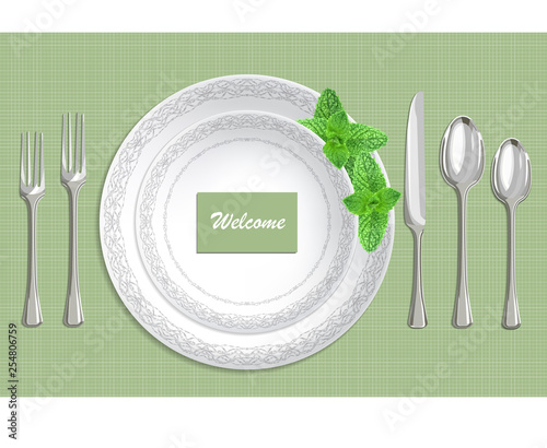 Table setting with plate, spoon, knife and fork on a green fabric background