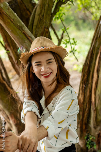Women white skin lovely brown hair wearing a basketry hat brown red lip wear white shirt wearing black pants women sit poses photography portrait under the tree In the garden.