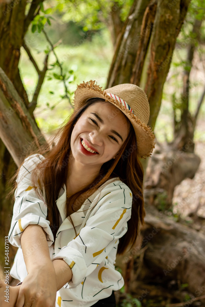 Women white skin lovely brown hair wearing a basketry hat brown red lip wear white shirt wearing black pants women sit poses photography portrait under the tree In the garden.