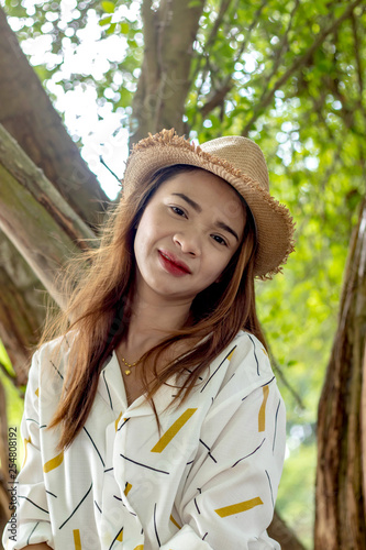 Women white skin lovely brown hair wearing a basketry hat brown red lip wear white shirt wearing black pants women sit poses photography portrait under the tree In the garden.