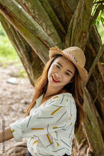 Women white skin lovely brown hair wearing a basketry hat brown red lip wear white shirt wearing black pants women sit poses photography portrait under the tree In the garden.
