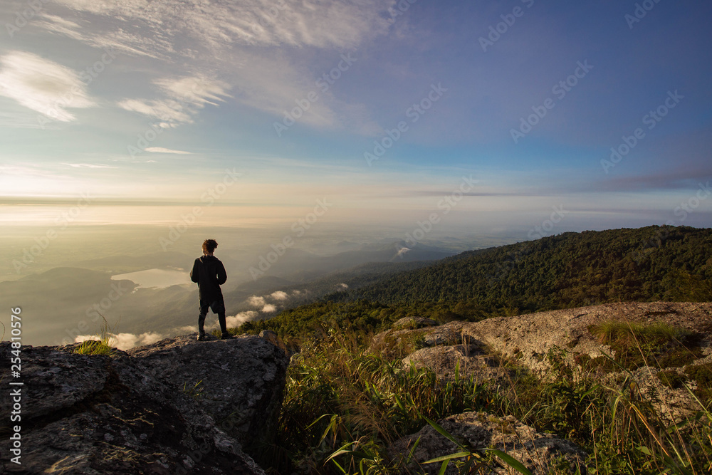 Silhouettes of man standing on top mountain and looking sunset.