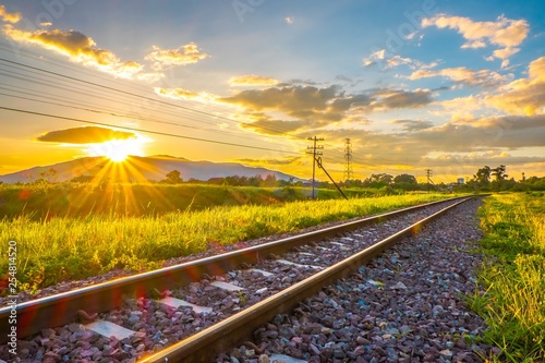 Chiang Mai Railway Track in the countryside with Green Grass along the way in Summer Evening before Sunset. Wallpaper Background of Railroad in Late Afternoon