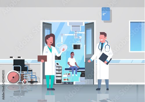 doctors couple discussing in hospital corridor with wheelchair open door to surgery room african man sitting operating table modern clinic interior flat full length horizontal