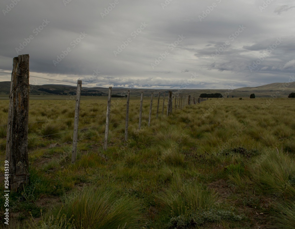 un alambrado se extiende hacia el horizonte en un prado enmarcado por montañas