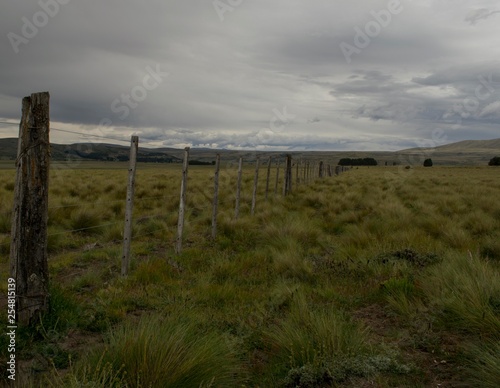 un alambrado se extiende hacia el horizonte en un prado enmarcado por montañas
