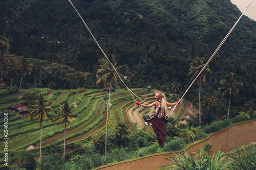Woman on Swing between palm trees with beautiful rice terrace landscape on background