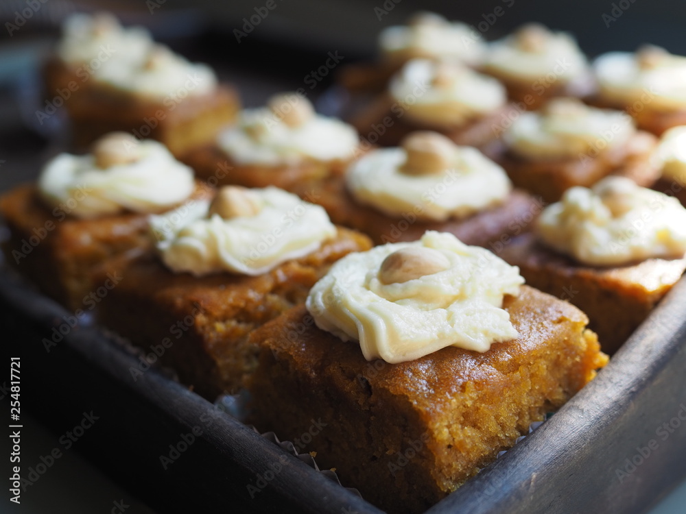 Slice of carrot cake with cream cheese frosting on wooden tray