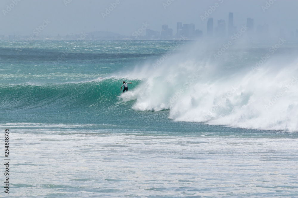 a surfer catching wave tropical emerald green ocean from Kirra beac and behind city of surfers paradise Australia 
