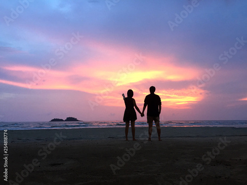 Couple hold each other hand at the beach under sunset. What a perfect moment under the sunset sky!