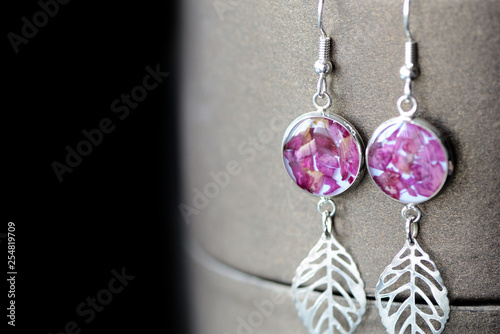 Dangle resin earrings with rose petals on a dark background close up