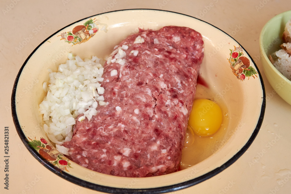 fresh beef and pork minced meat sprinkled with white onions and chicken egg for making cutlets and schnitzel in a yellow iron plate. meat patties