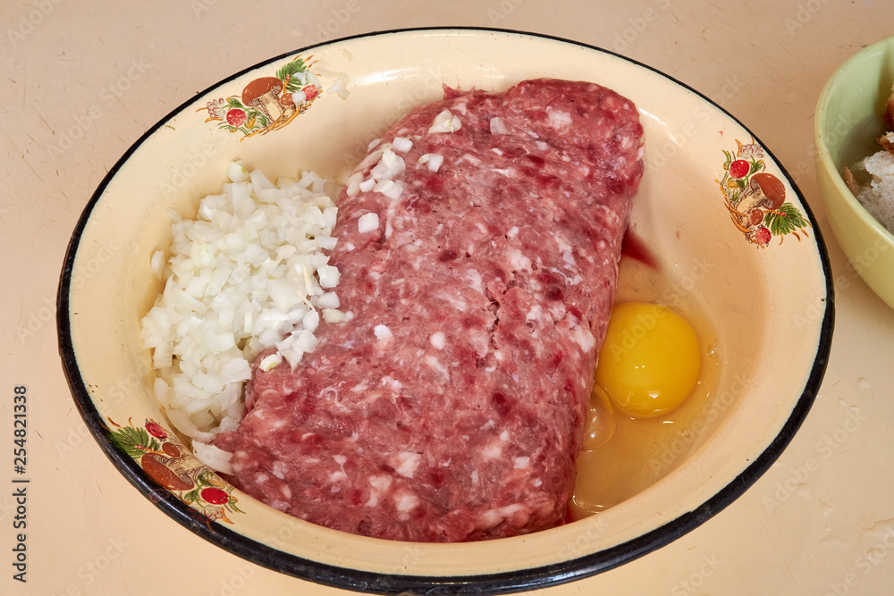 fresh beef and pork minced meat sprinkled with white onions and chicken egg for making cutlets and schnitzel in a yellow iron plate. meat patties. On the kitchen table. fresh beef and pork minced meat sprinkled with white onions and chicken egg for making cutlets and schnitzel in a yellow iron plate. meat patties. On the kitchen table.
