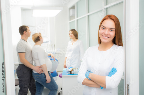 Fototapeta Naklejka Na Ścianę i Meble -  Young beautiful woman doctor stands against the background of patients in the clinic. Patients married couple, woman pregnant