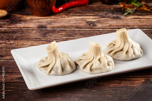 The concept of Georgian cuisine. Khinkali from white dough with meat. Serving dishes in Georgian restaurant on a white plate, on a wooden table. Background image. copy space