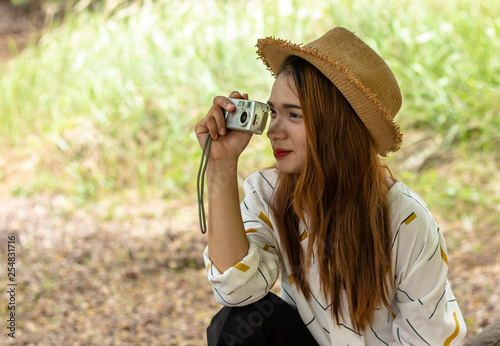 Women tourists women white skin lovely brown hair wearing a basketry hat wear white shirt wearing black pants in hand have a camera traipse photograph nature.