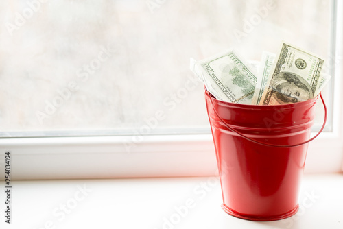 Dollar bills in red pail. on white window.light background. place for text. top view. a lot of money photo