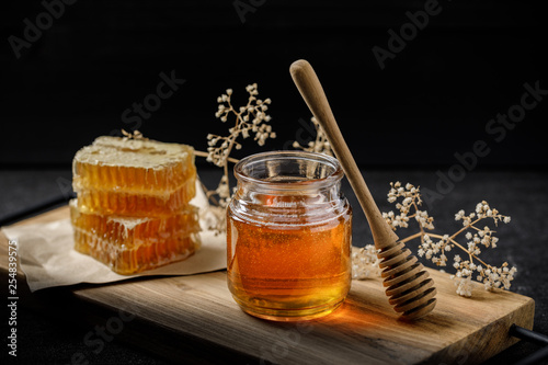 Honeycomb with honey dipper and dry flower on black background, bee products by organic natural ingredients concept