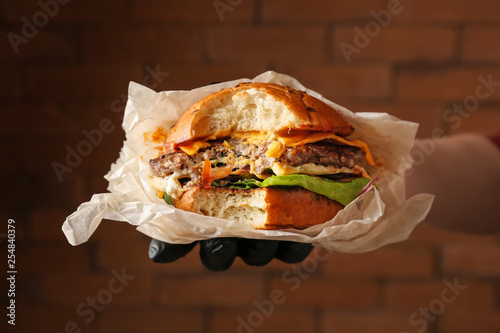 Принти на полотні Female hand holding tasty bitten burger on color background