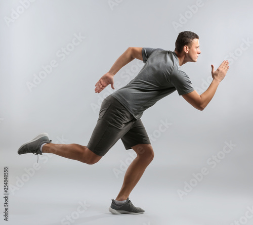 Sporty young man running against grey background