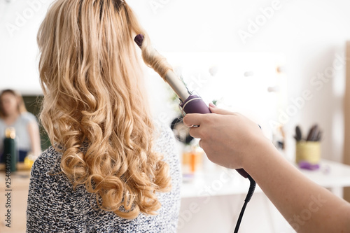 Quadro em tela Hairdresser curling long hair of young woman in salon