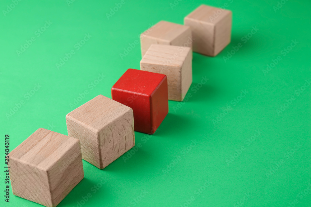 Red cube among wooden ones on color background. Concept of uniqueness