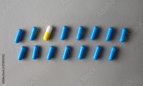 Yellow pill among blue ones on grey background. Concept of uniqueness