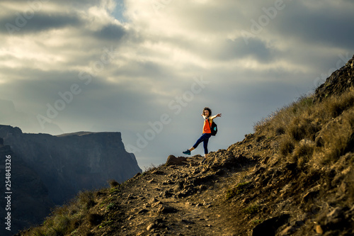 Young and attractive girl in orange shirt and blue leggings is hiking by the tourist s trail on Madeira island  Portugal. Sunny day.