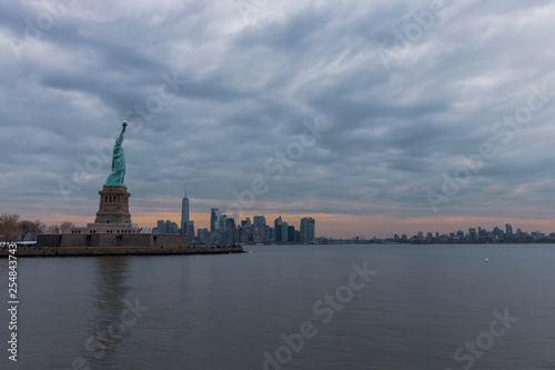 View of New York City skyline and Statue of Liberty with dramatic sky at dusk, New York, USA