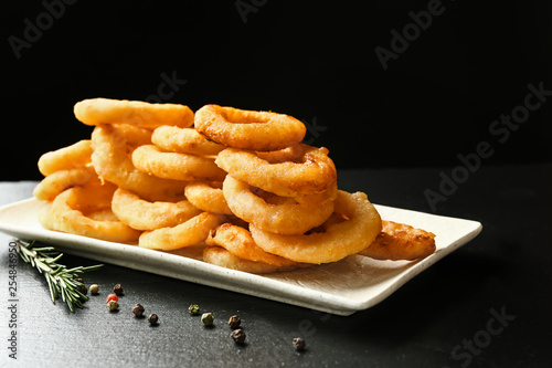 Plate with tasty onion rings on dark background