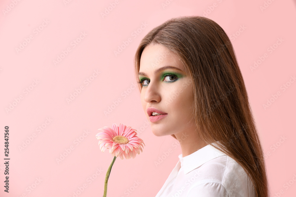 Beautiful young woman with bright makeup and flower on color background