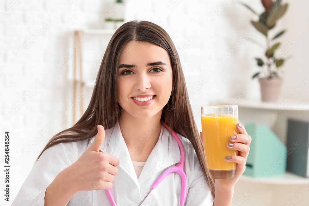 Portrait of female nutritionist with glass of juice showing thumb-up in her office Portrait of female nutritionist with glass of juice showing thumb-up in her office