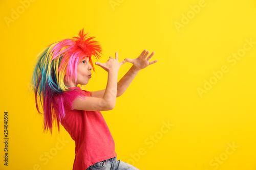 Funny little girl in wig on color background. April fools' day celebration