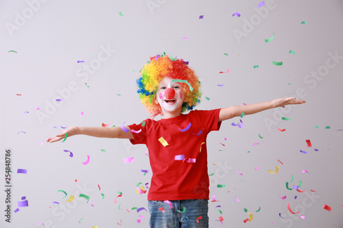 Little boy in funny disguise and falling confetti on light background. April fools' day celebration