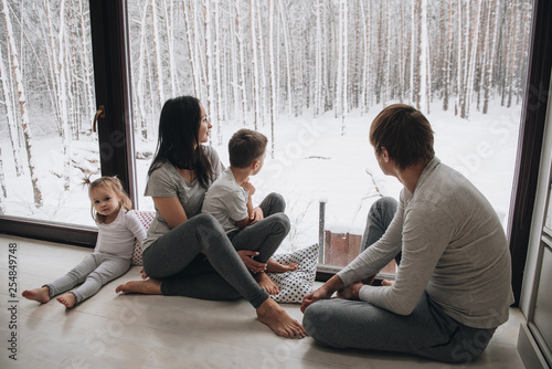 Family at home in pajamas. Daughter and son. Wake up in the morning. Hugging and kissing, looking out the window. Beautiful winter outside the window. Large windows to floor. Nice view from window.